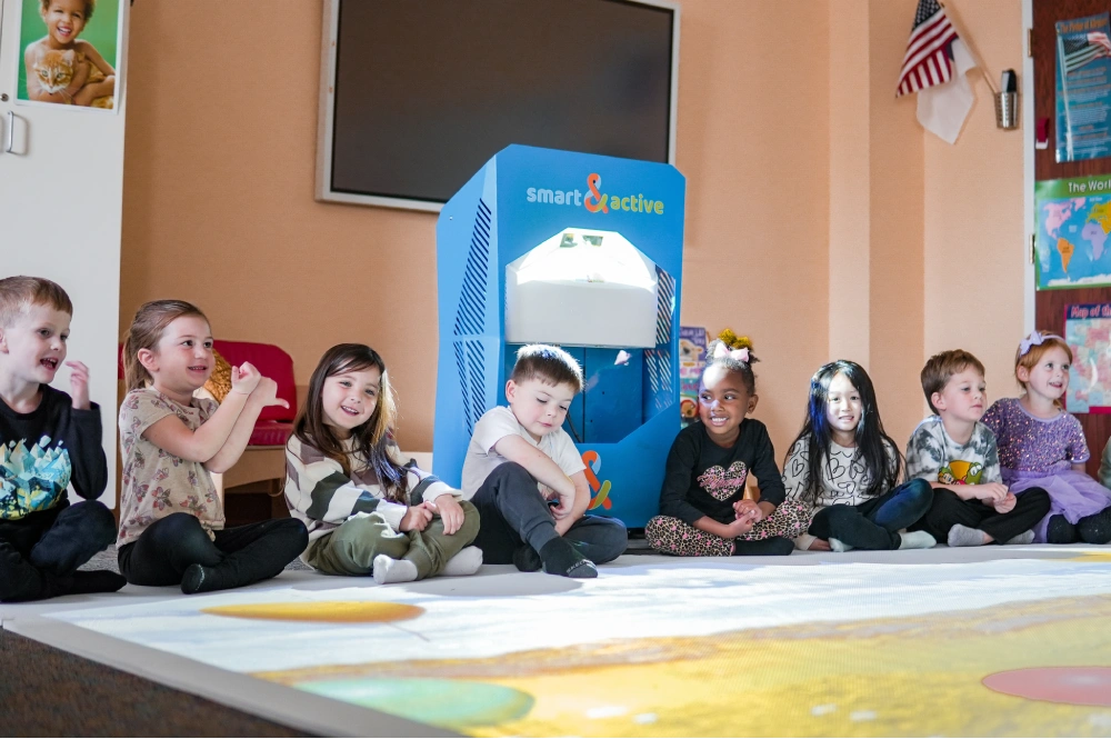 Children sit in a semicircle on a projection floor with bright animation