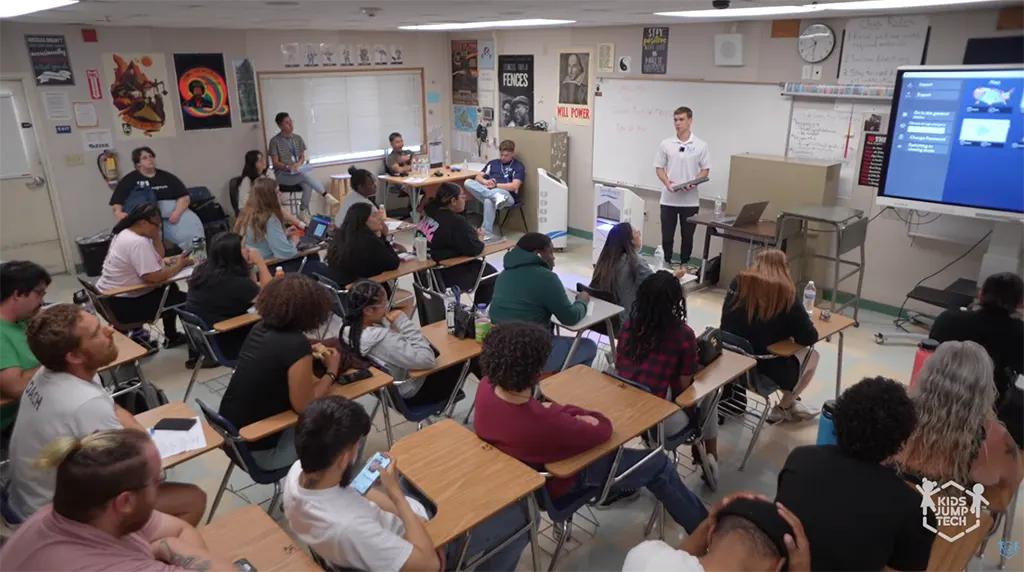 Students attending a classroom lecture, listening to an instructor presenting educational material on a large interactive display screen