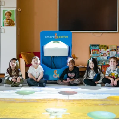 Group of children sitting around an Interactive Floor System with educational games projected on the floor